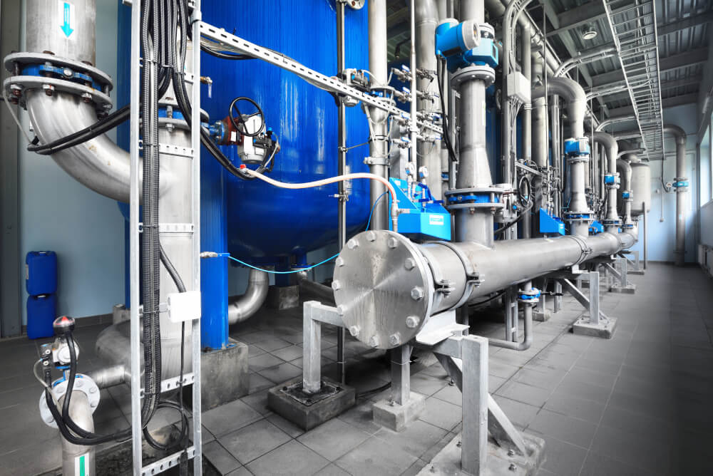 Large industrial water treatment and boiler room. Shiny steel metal pipes and blue pumps and valves.
